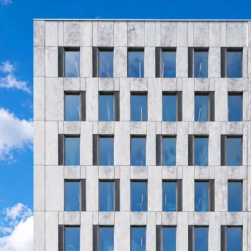 Contemporary concrete office tower facade with a regular grid of tall rectangular windows under a blue sky.